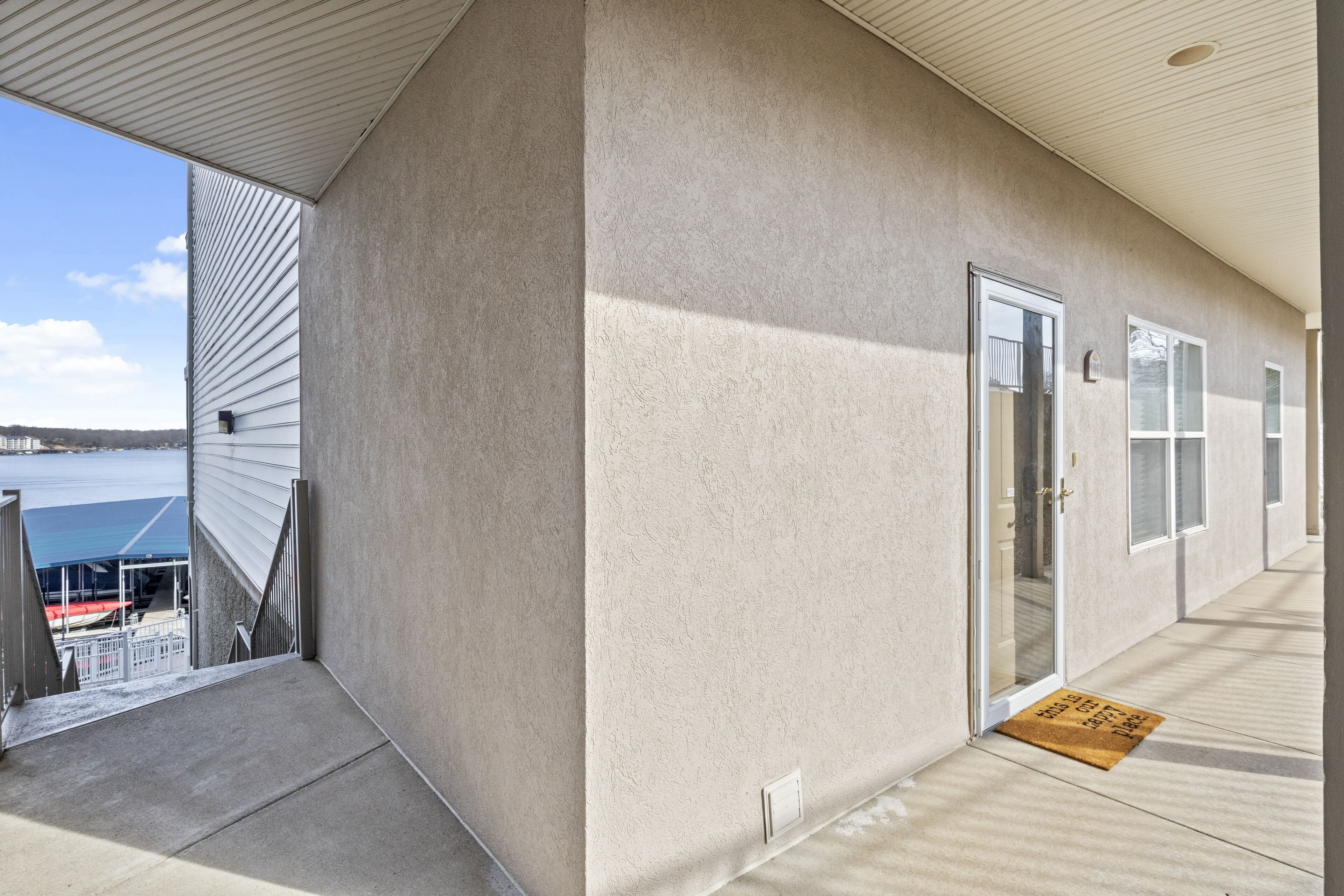 A covered outdoor area with a concrete floor, a door with a glass panel, and a doormat.