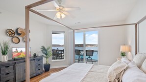 Un dormitorio amplio con una cama grande, un ventilador de techo y vistas al agua a través de ventanas panorámicas.