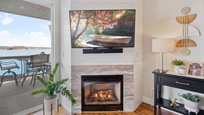 Una sala de estar con chimenea, un televisor montado encima y vistas a un balcón con mobiliario exterior.