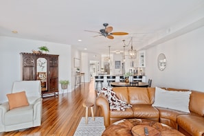 A spacious living room with a leather sofa, a white armchair, and a wooden cabinet.