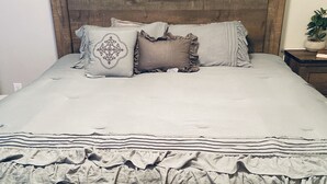 Een net opgemaakt bed met een gefronste onderrok, een houten hoofdbord en een ronde wandklok.