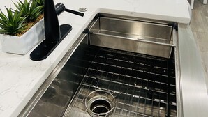 Een keuken met een wit aanrecht, een zwarte kraan, een roestvrijstalen spoelbak en een potplant.