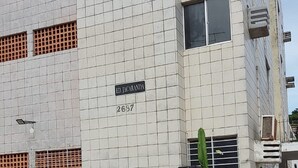 A building with a tiled facade, a sign reading "ED. JACARANDA 2637", and a black metal fence in the foreground. - Apartment (Jaboatão dos Guararapes)