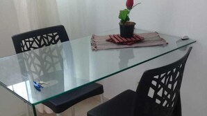 A glass-top dining table with two black chairs, a potted plant, and a small table lamp. - Apartment (Jaboatão dos Guararapes)