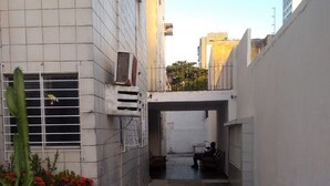 A narrow alleyway with a tiled floor, a cactus plant, and a small garden with red flowers. There is a metal ladder leaning against a wall and a bicycle parked on the right. - Apartment (Jaboatão dos Guararapes)
