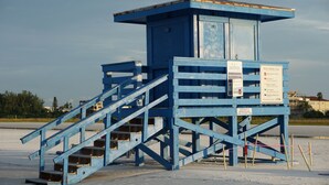 Una torre di salvataggio con un cartello che indica avvisi sulla spiaggia e la distanza minima dalla postazione del bagnino.