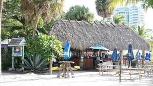 Un bar sulla spiaggia con tetto di paglia, posti a sedere all'aperto e ombrelloni.