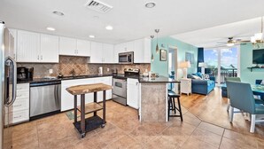 Una cocina moderna con armarios blancos, una isla central y un área de comedor con mobiliario azul.