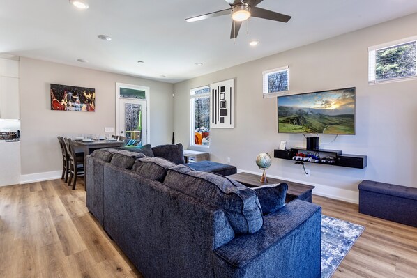 A modern living room with a sectional sofa, a flat-screen TV, and a dining area with a table and chairs.
