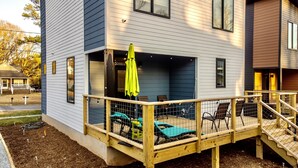 Une maison à deux étages dotée d’une terrasse en bois, d’un espace salon extérieur et d’un patio couvert.