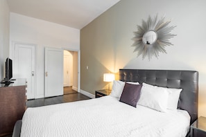 Una habitación de hotel con cama, mesita de noche, lámpara, televisor y espejo instalado en la pared.