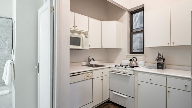 A compact kitchen with white cabinets, a microwave, a stove, and a sink. - Timeless NYC Living | UWS | Pet-Friendly (New York)