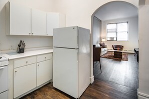 Una cocina con armarios blancos, un refrigerador blanco y un comedor con una silla y una mesa.