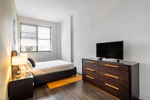 Una camera da letto con un letto, una TV su una cassettiera, una finestra con persiane e un condizionatore d'aria.