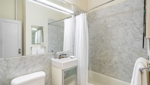 A bathroom with a toilet, sink, mirror, shower curtain, and bathtub. - Timeless NYC Living | UWS | Pet-Friendly (New York)