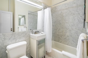 Un baño con inodoro, lavabo, espejo, cortina de ducha y bañera.