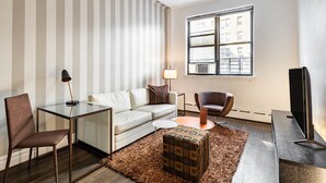 A modern living room with a sofa, armchair, glass coffee table, and a television. - Timeless NYC Living | UWS | Pet-Friendly (New York)