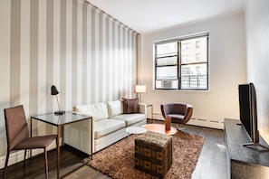 Una sala de estar moderna con sofá, sillón, mesa de centro de vidrio y televisor.