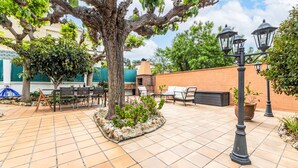Un patio exterior con pared de ladrillo, un árbol grande, mobiliario para exteriores y una zona de barbacoa de ladrillo.
