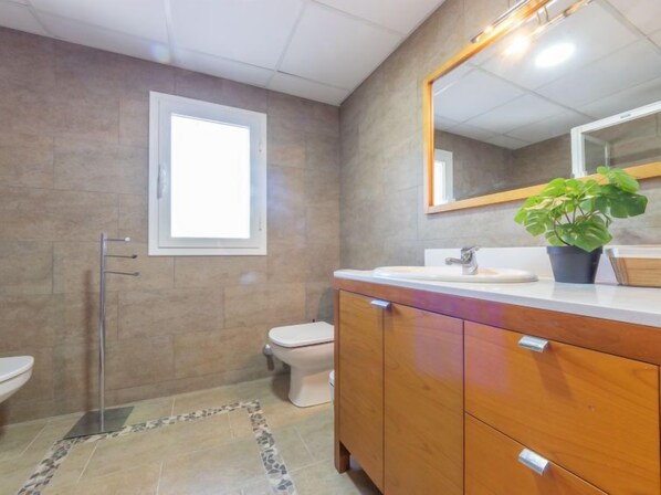A bathroom with a toilet, sink, and mirror. There is a window above the toilet and a plant on the sink counter. - Torre del Sol by Interhome (Torredembarra)