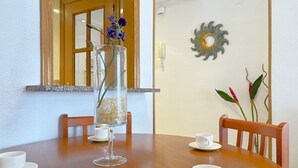A dining table with a clear glass vase containing flowers, two white cups, and a wooden chair.
