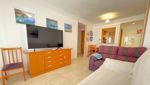 A living room with a television, a sofa, a chair, and a wooden cabinet.