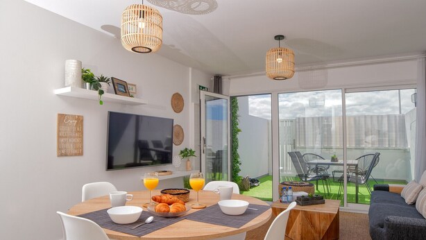 Un espace repas moderne avec une table ronde, des chaises blanches et une table préparée pour le petit-déjeuner, avec des croissants et du jus d’orange.