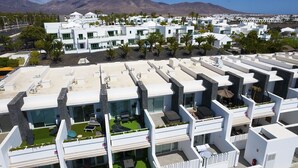 Un complexe hôtelier moderne composé de plusieurs bâtiments blancs, doté de terrasses sur les toits aménagées avec du mobilier d’extérieur, et offrant une vue imprenable sur les montagnes.