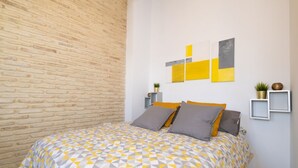 A bedroom with a brick wall, a bed with a geometric patterned bedspread, two pillows, and two wall-mounted artworks. - Triana Penthouse by Sevillaluxurysuites (Sevilla)