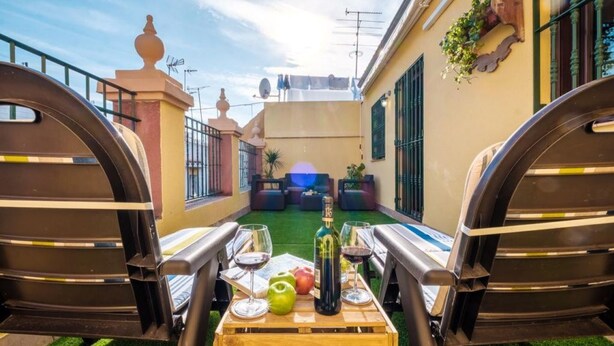 A cozy outdoor seating area with a wooden table set for two, featuring a bottle of wine, glasses, and a green apple. - Triana Penthouse by Sevillaluxurysuites (Sevilla)