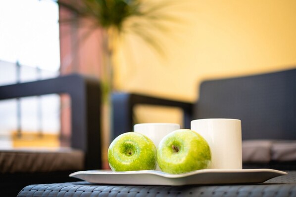 Une table avec une assiette contenant deux pommes vertes et deux tasses blanches.