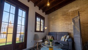 A modern living room with a glass coffee table, a grey sofa with patterned cushions, a wooden-framed window, and a brick wall. - Triana Penthouse by Sevillaluxurysuites (Sevilla)