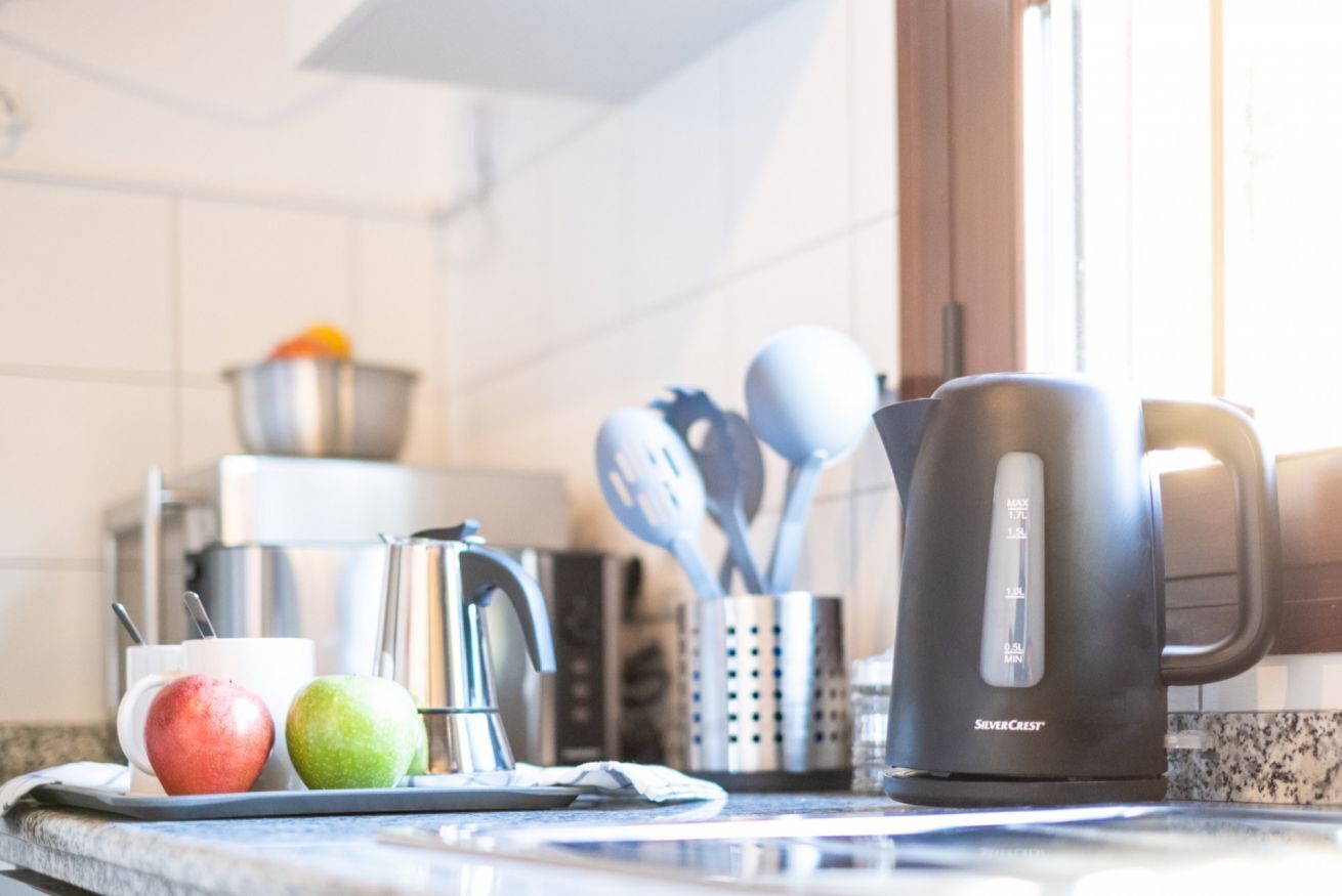 A kitchen counter with a coffee maker, a cup, and two apples.