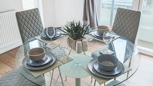 A dining table set for four with glass tops, cushioned chairs, and a potted plant. - Duplex Apartment • Balcony • FreeParking • SmartTV (Newport Pagnell)