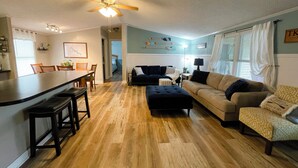 A spacious living area with a kitchen, a dining table, and a bar area. There is a ceiling fan, a lamp, and a couch. - Quiet Cove with Big Water Views (Ridgeway)