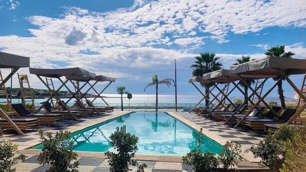 A pool area with lounge chairs and umbrellas, a clear sky, and a view of the sea. - Jonium Hotel (Pulsano)