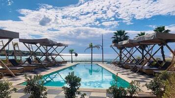Zona de piscina con sillas de descanso y sombrillas, cielo despejado y vista al mar.