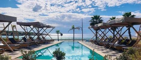 A pool area with lounge chairs and umbrellas, a clear sky, and a view of the sea.