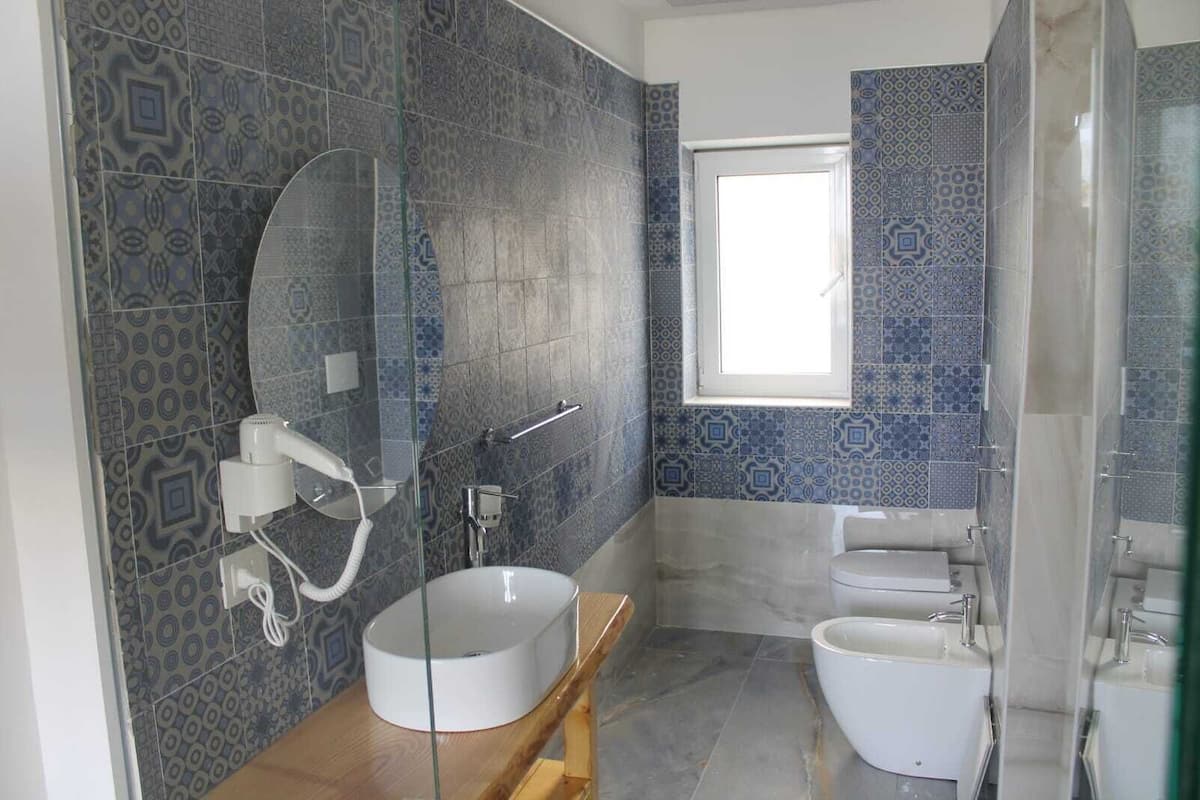 Une salle de bain avec des carreaux décorés, un lavabo rond, des toilettes et une fenêtre.