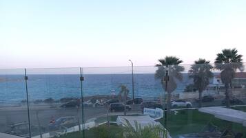 Un balcón con vistas al mar, una piscina y sillas blancas.