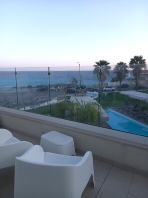 Varanda com vista para o mar, piscina e cadeiras brancas.