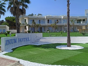 El exterior del Hotel Jonium, con un césped cuidado, palmeras y un cielo azul despejado.