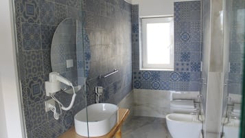 Une salle de bain avec des carreaux décorés, un lavabo rond, des toilettes et une fenêtre.