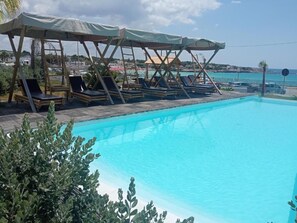 A swimming pool with lounge chairs and a covered seating area. - Jonium Hotel (Pulsano)