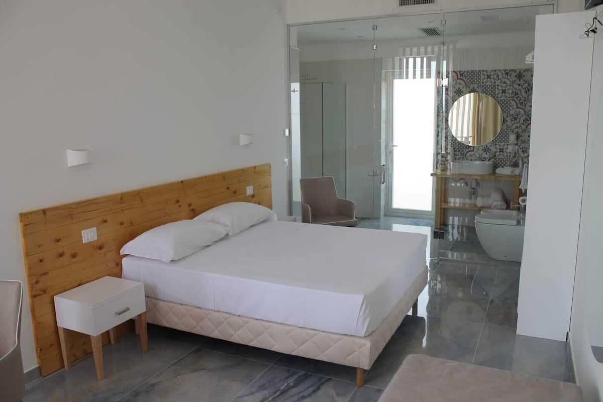 Une chambre moderne avec une tête de lit en bois, un lit simple, une table de chevet et une salle de bain visible à travers une porte ouverte.