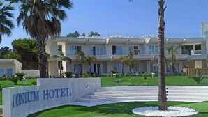 The exterior of the Jonium Hotel with a well-maintained lawn, palm trees, and a clear blue sky. - Jonium Hotel (Pulsano)