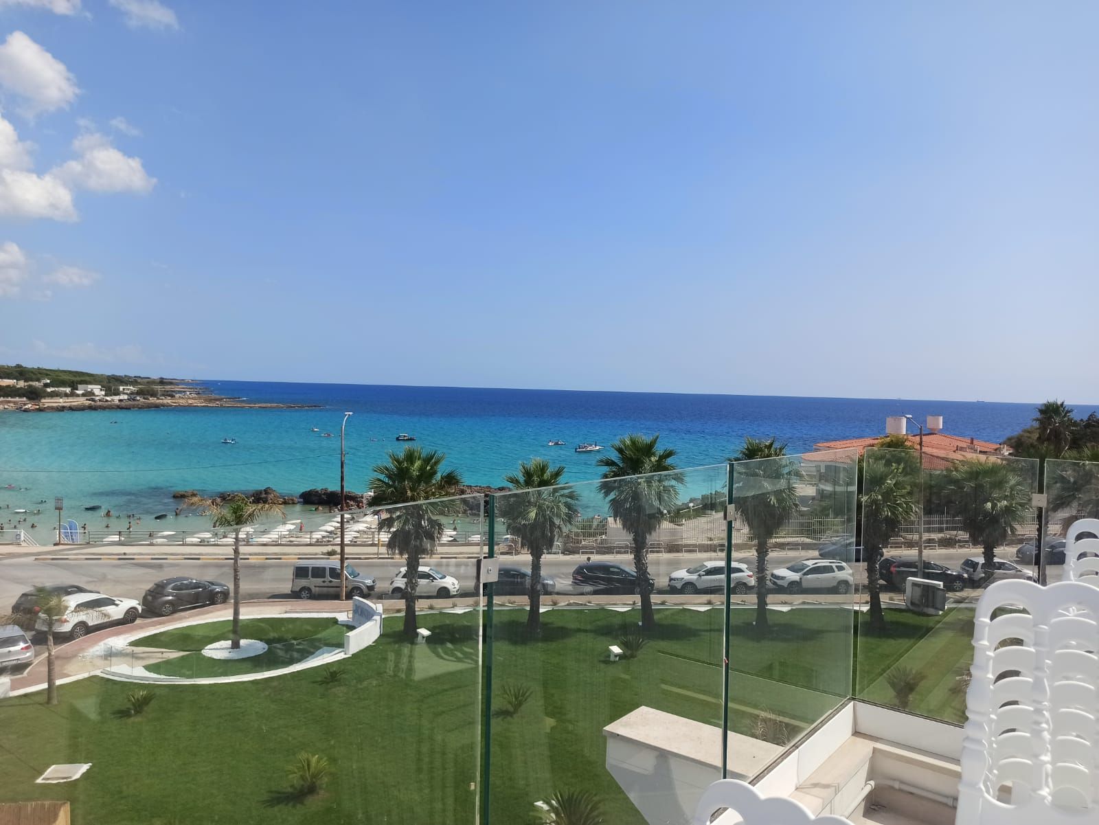 Vista de una zona costera con cielo despejado, una playa y coches aparcados.