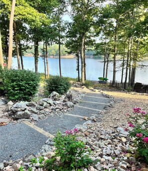 A stone pathway leading to a lake, surrounded by trees and rocks.