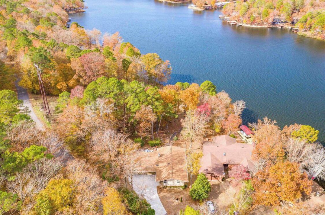 Eine Luftaufnahme eines Sees mit einem Grundstück, auf dem ein Haus von herbstlich gefärbten Bäumen umgeben ist.