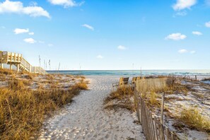 A sandy beach path leading to a wooden staircase and beach chairs.